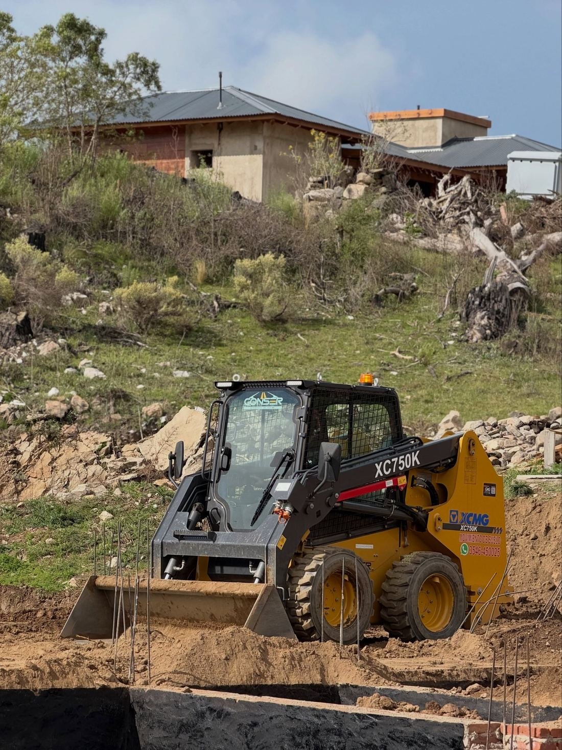 Minicargadora XCMG XC750K de CONSER trabajando junto a una casa en construcción